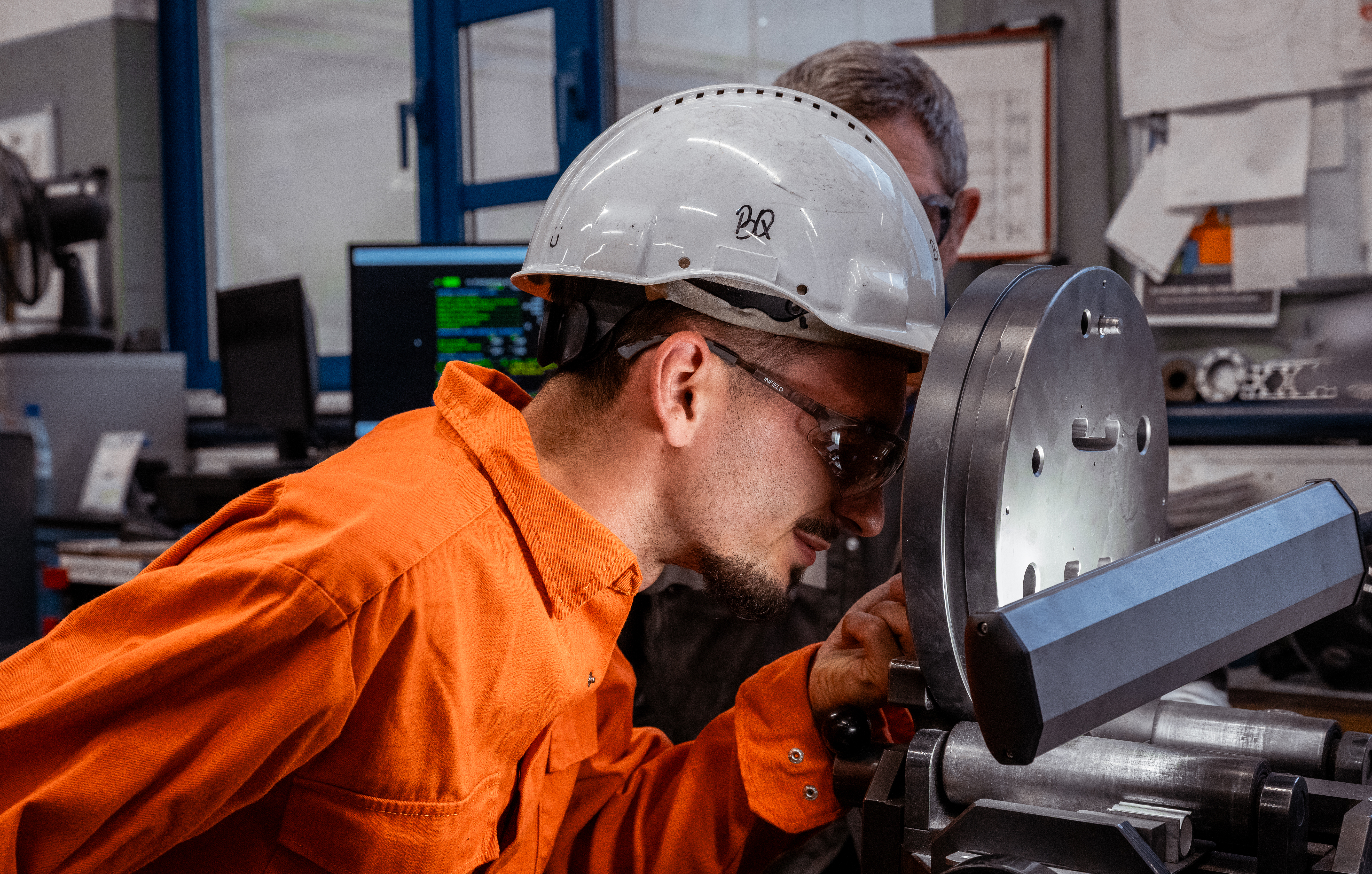 a man wearing a hard hat and glasses looking at a machine